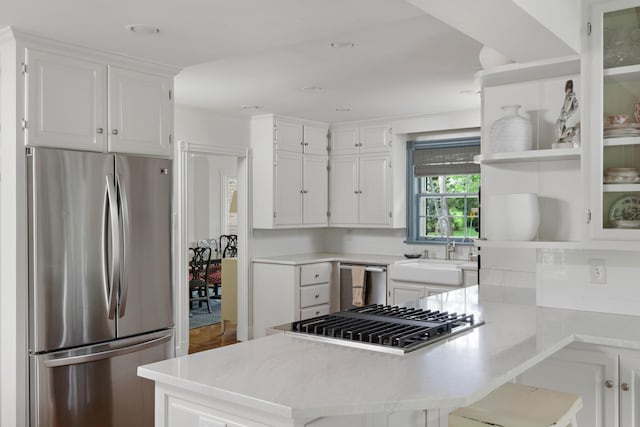 kitchen with light countertops, appliances with stainless steel finishes, white cabinets, a sink, and a peninsula