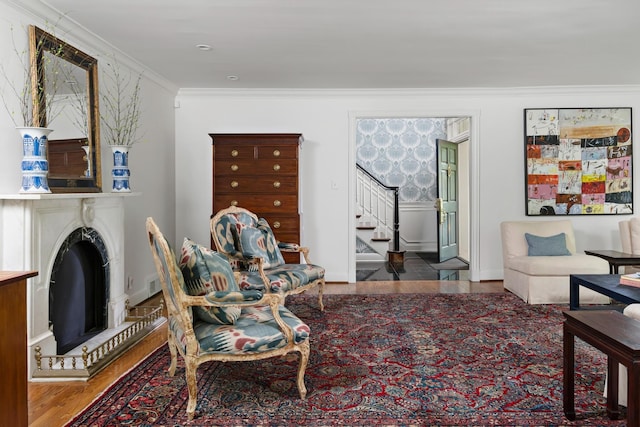 living area featuring baseboards, a fireplace with raised hearth, stairway, wood finished floors, and crown molding