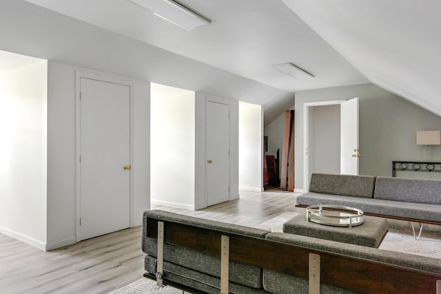 interior space featuring light wood finished floors, baseboards, and vaulted ceiling