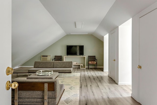 living area with lofted ceiling, light wood-type flooring, baseboards, and a wall mounted air conditioner