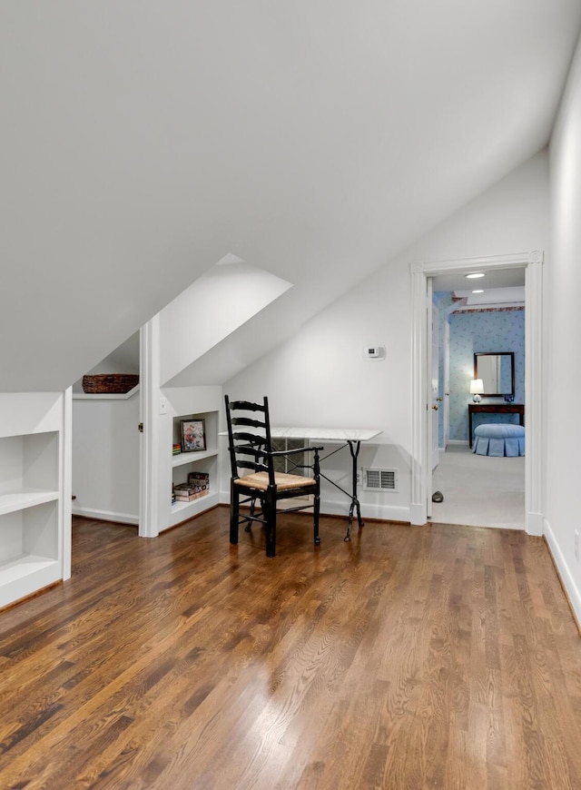 office space featuring built in shelves, lofted ceiling, visible vents, wood finished floors, and baseboards