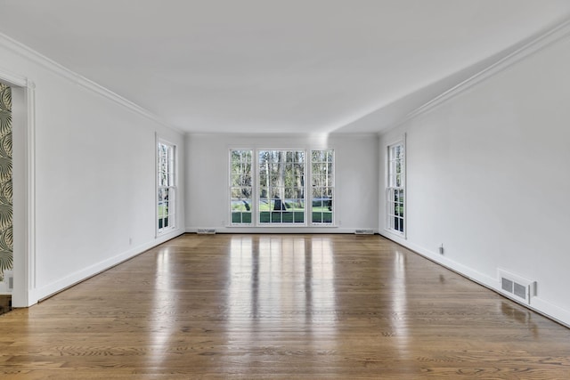 unfurnished room featuring a wealth of natural light, ornamental molding, wood finished floors, and visible vents