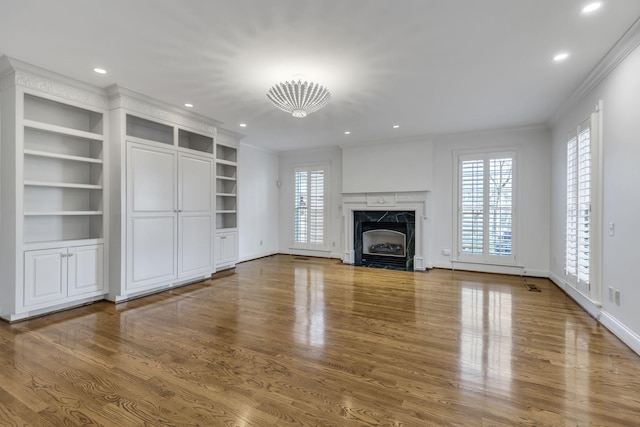 unfurnished living room with crown molding, a fireplace, wood finished floors, and a healthy amount of sunlight