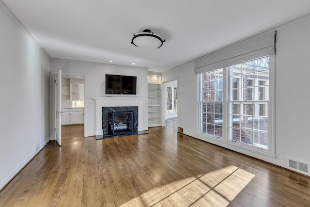 unfurnished living room with built in shelves, a fireplace, visible vents, wood finished floors, and baseboards