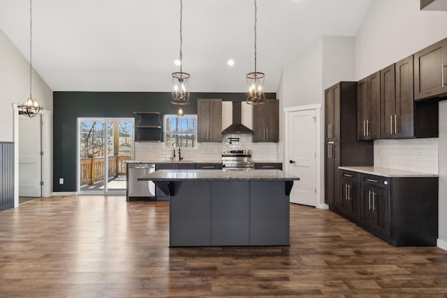 kitchen featuring dark brown cabinetry, stainless steel appliances, a kitchen island, a sink, and wall chimney range hood