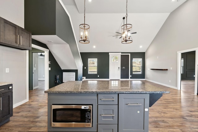 kitchen with wood finished floors, open floor plan, stainless steel microwave, and light stone countertops