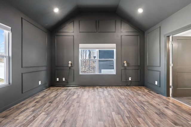 interior space with vaulted ceiling, a decorative wall, and wood finished floors