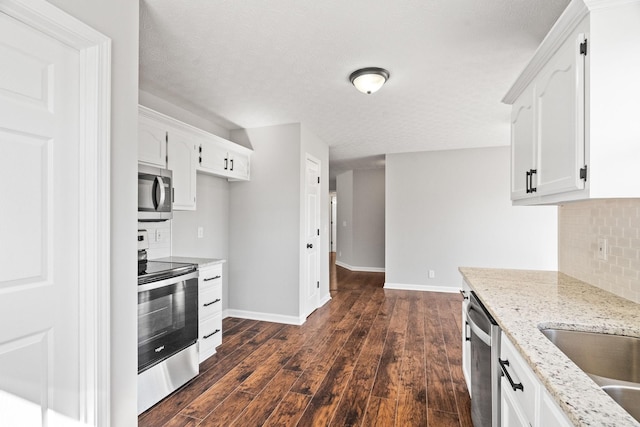 kitchen with appliances with stainless steel finishes, dark wood finished floors, light stone counters, and white cabinets