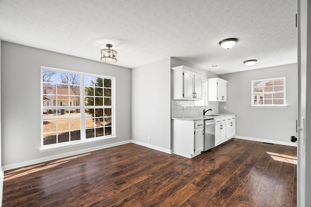 kitchen with dark wood-style flooring, tasteful backsplash, light countertops, stainless steel dishwasher, and a sink