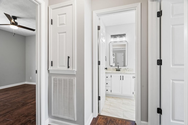 hallway with a textured ceiling, dark wood-type flooring, a sink, visible vents, and baseboards