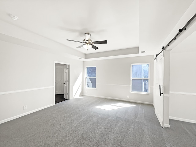 unfurnished bedroom with a barn door, baseboards, a raised ceiling, ceiling fan, and carpet flooring