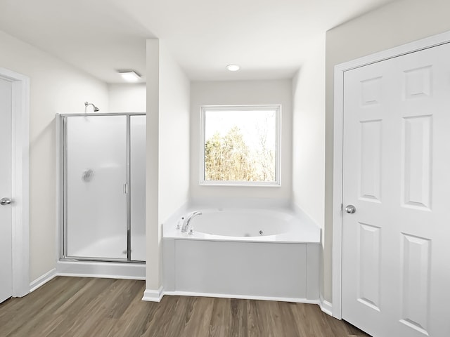 bathroom with wood finished floors, a stall shower, a garden tub, and baseboards