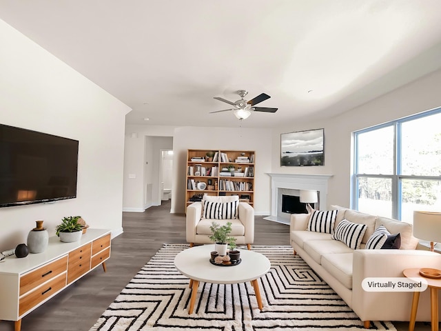 living area featuring a fireplace with flush hearth, dark wood finished floors, baseboards, and ceiling fan