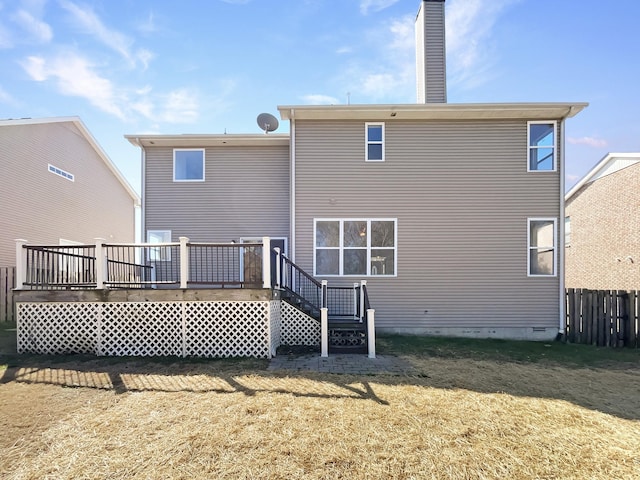 back of house featuring a deck, a chimney, fence, and a lawn