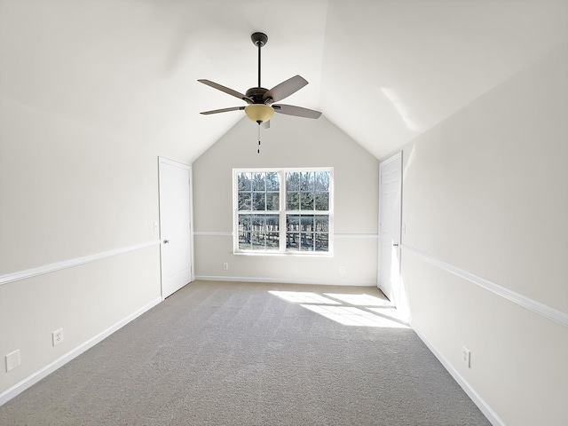 carpeted empty room featuring a ceiling fan, vaulted ceiling, and baseboards