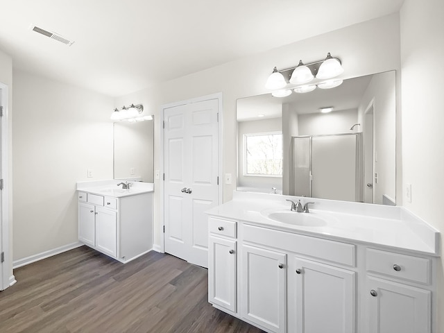 bathroom featuring wood finished floors, two vanities, a sink, and visible vents