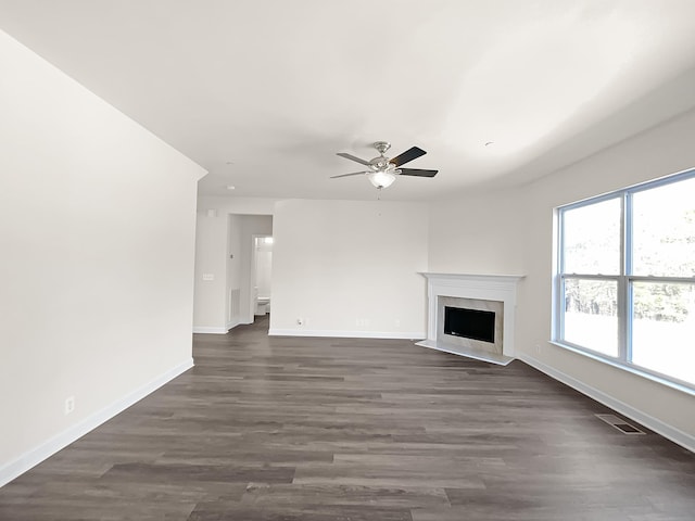 unfurnished living room with ceiling fan, a premium fireplace, visible vents, baseboards, and dark wood finished floors