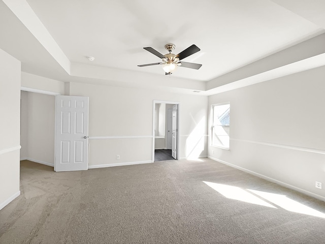 carpeted empty room with a ceiling fan, a tray ceiling, and baseboards