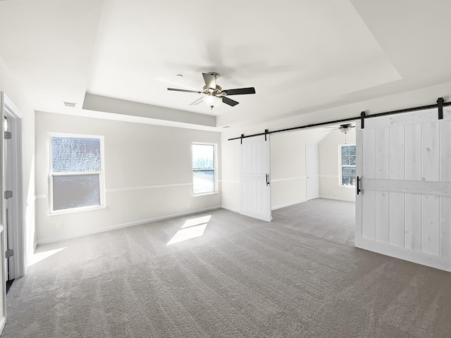 carpeted empty room with a tray ceiling, visible vents, a barn door, a ceiling fan, and baseboards