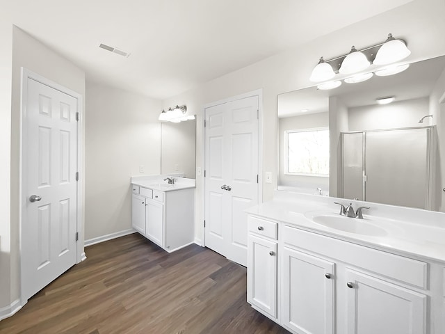 full bathroom with wood finished floors, two vanities, a sink, visible vents, and a shower stall