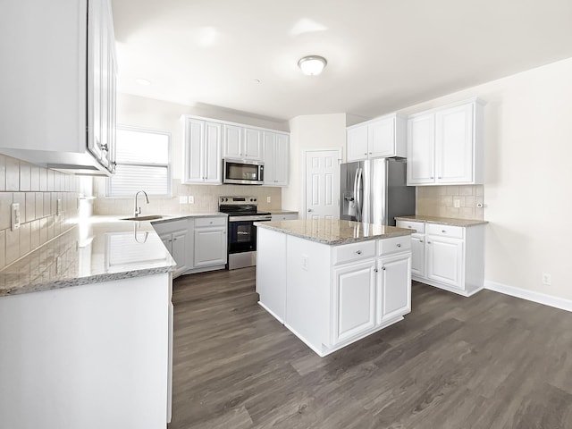 kitchen with light stone counters, a center island, stainless steel appliances, white cabinetry, and a sink