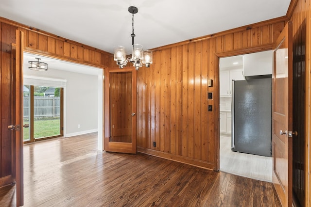 unfurnished dining area featuring a notable chandelier, wood walls, baseboards, and wood finished floors