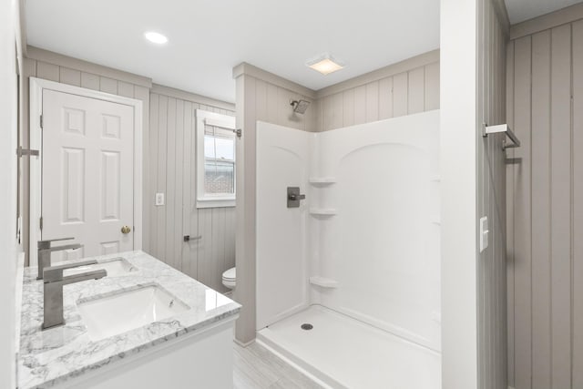 bathroom with toilet, double vanity, walk in shower, and a sink