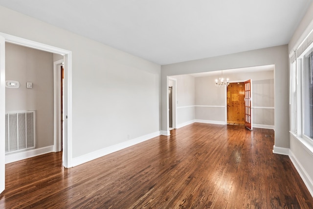 empty room featuring baseboards, visible vents, dark wood-type flooring, and a notable chandelier