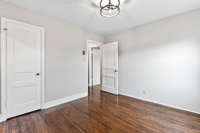 unfurnished bedroom with an inviting chandelier, baseboards, and dark wood-type flooring