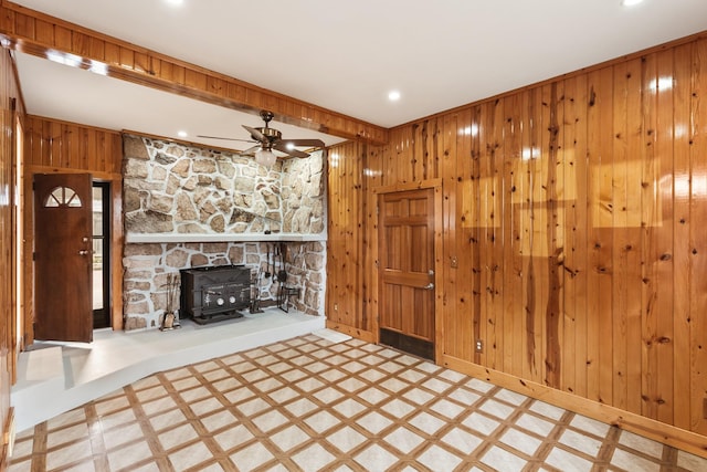 unfurnished living room with recessed lighting, a wood stove, ceiling fan, wooden walls, and baseboards