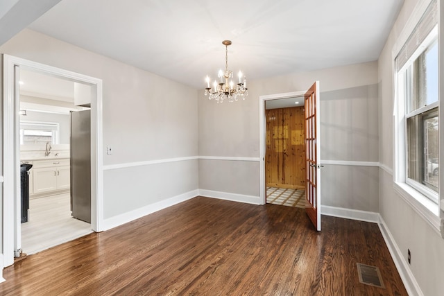 unfurnished dining area featuring a chandelier, a sink, wood finished floors, visible vents, and baseboards