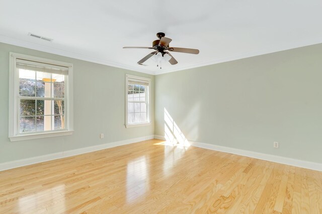 spare room featuring wood finished floors, a ceiling fan, visible vents, baseboards, and ornamental molding