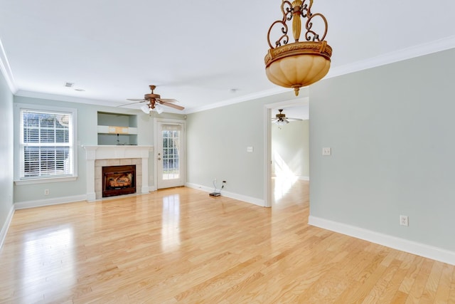 unfurnished living room with light wood-style floors, a tiled fireplace, baseboards, and crown molding