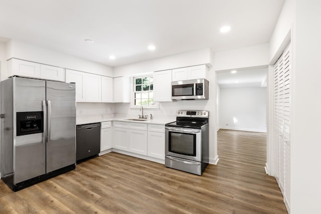 kitchen featuring wood finished floors, appliances with stainless steel finishes, a sink, and white cabinets