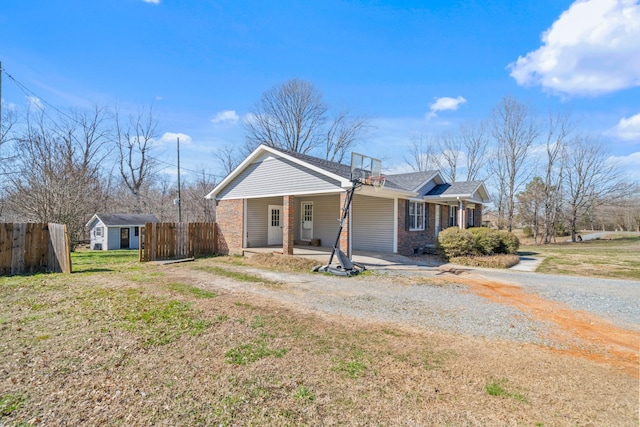 view of front facade with an outbuilding, a porch, brick siding, fence, and gravel driveway