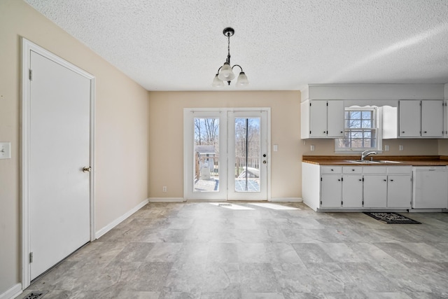 kitchen featuring hanging light fixtures, white cabinets, a sink, dishwasher, and baseboards