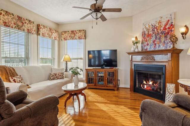 living room featuring a textured ceiling, ceiling fan, a glass covered fireplace, and wood finished floors