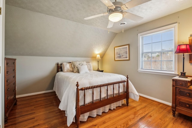 bedroom with lofted ceiling, a textured ceiling, baseboards, and wood finished floors