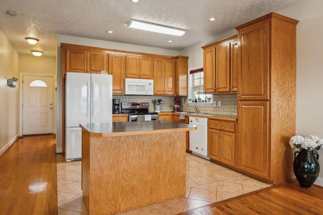 kitchen featuring tasteful backsplash, white appliances, light tile patterned flooring, and a kitchen island