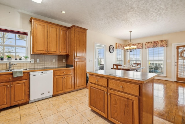 kitchen featuring brown cabinetry, dishwasher, backsplash, a notable chandelier, and a sink