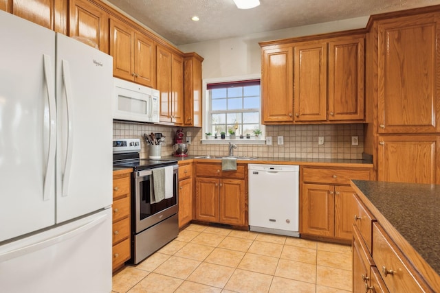 kitchen with white appliances, decorative backsplash, brown cabinets, a sink, and light tile patterned flooring