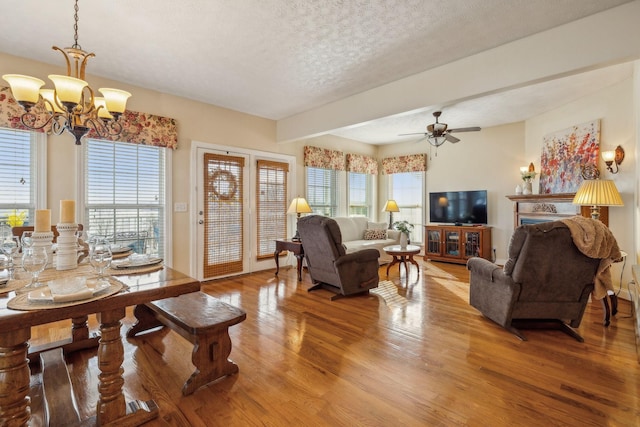 living room featuring ceiling fan with notable chandelier, a textured ceiling, and wood finished floors