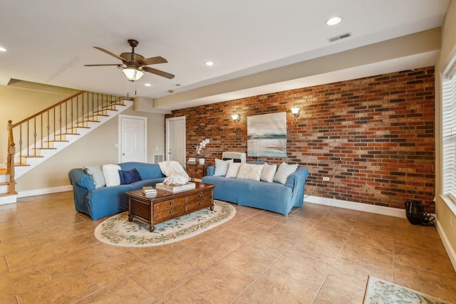 living area with ceiling fan, brick wall, visible vents, baseboards, and stairway