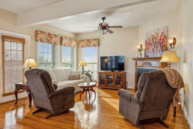 living area featuring a ceiling fan, a fireplace, baseboards, and wood finished floors