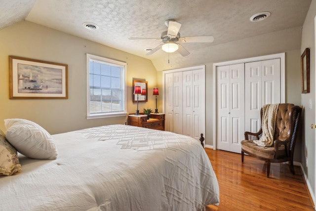 bedroom featuring visible vents, vaulted ceiling, multiple closets, and wood finished floors