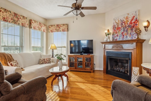 living area with a ceiling fan, a glass covered fireplace, a textured ceiling, and wood finished floors