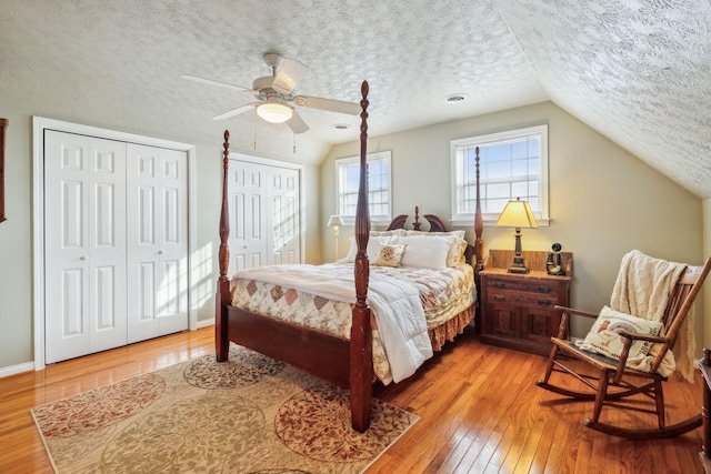 bedroom featuring wood-type flooring, a textured ceiling, vaulted ceiling, and multiple closets