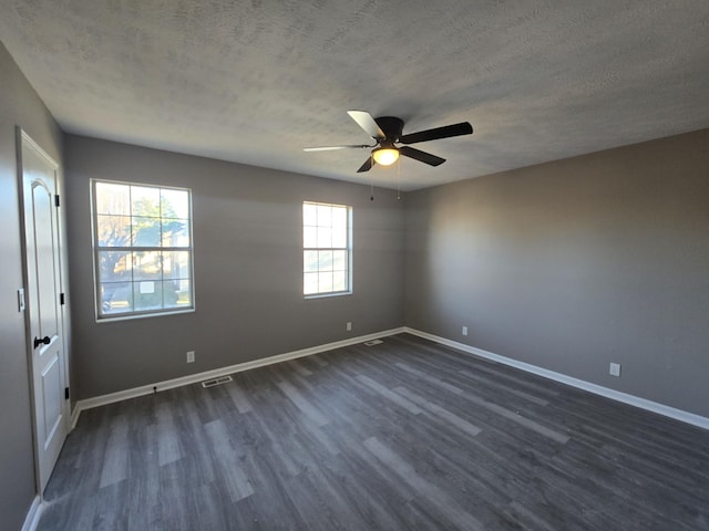 empty room with dark wood-style floors, a textured ceiling, visible vents, and baseboards