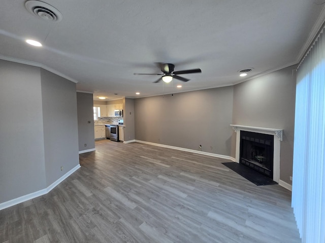 unfurnished living room with wood finished floors, a fireplace with flush hearth, baseboards, visible vents, and crown molding