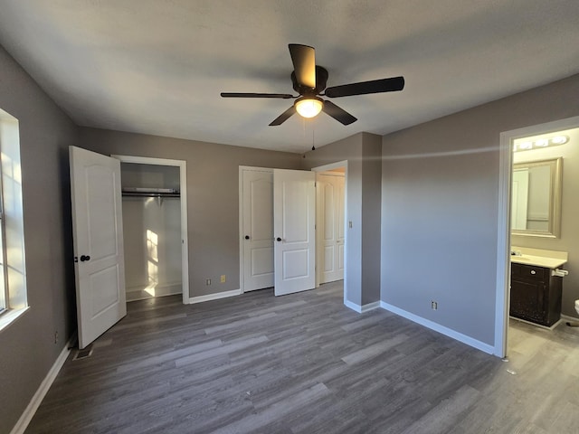 unfurnished bedroom featuring wood finished floors, baseboards, and two closets